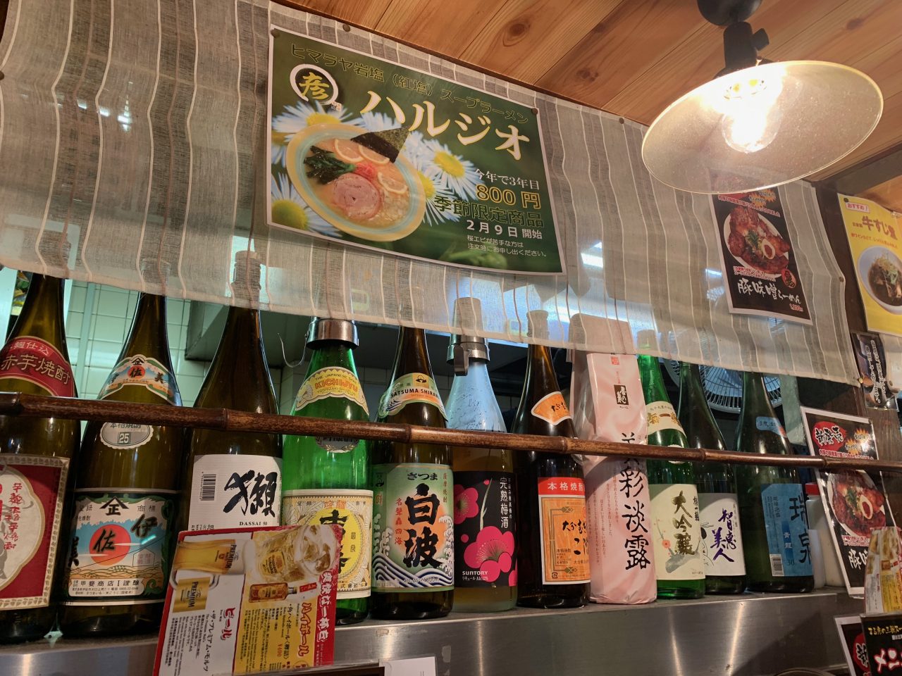 東京食品六本木店のカウンター席の写真。さまざまな種類の日本酒が並んでおり、壁には「ハルジオ」のポップが貼り付けられている。